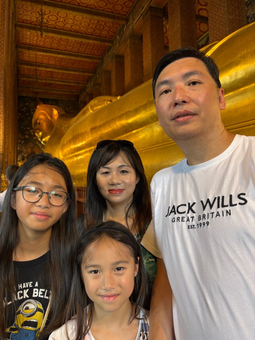 A family posing near the golden Reclining Buddha statue inside Wat Pho temple in Bangkok, Thailand.