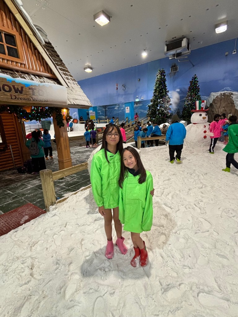 Two young girls dressed in winter jackets playing in the Snow Dome at Dream World Bangkok, surrounded by artificial snow and icy scenery.