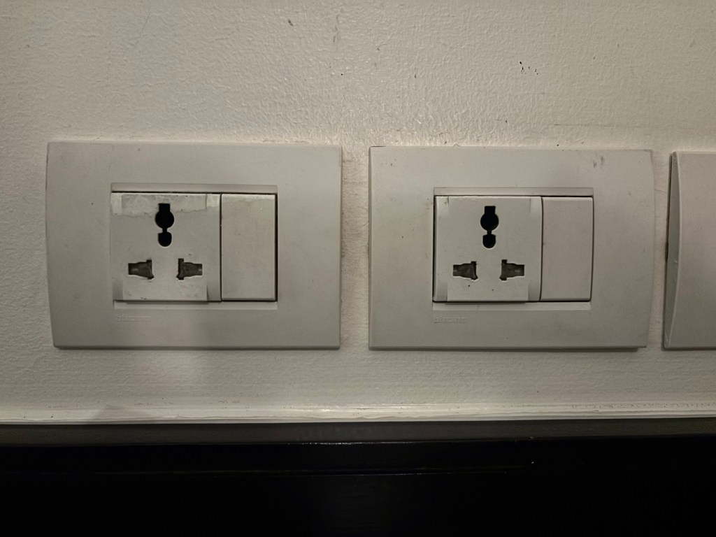 Multi‑region plug socket in a guest room at Mövenpick Hotel Sukhumvit 15 Bangkok, allowing guests to charge devices without a travel adaptor.