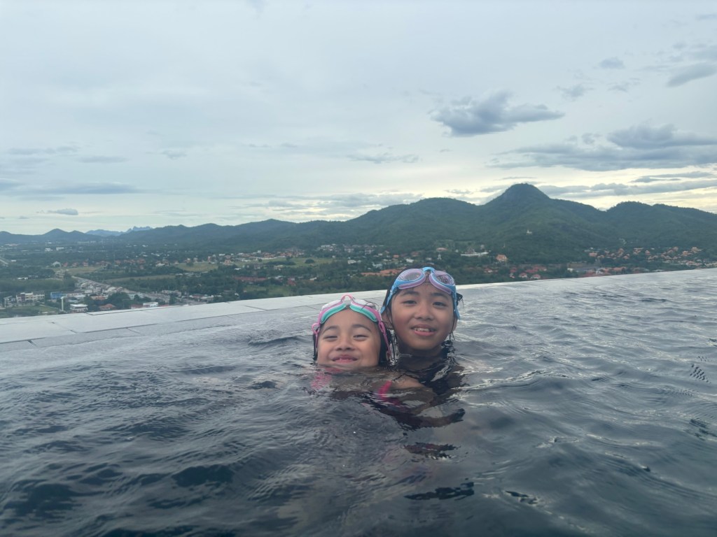 Child swimming in the rooftop infinity pool at Holiday Inn Resort Vana Nava Hua Hin, with scenic views over Hua Hin from the 26th floor.