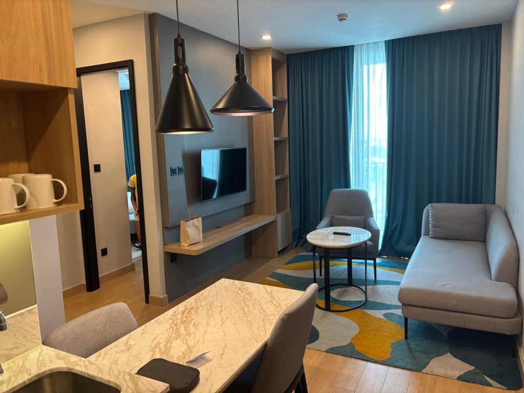 Living area in the two‑bedroom suite at Holiday Inn & Suites Siracha Laemchabang, with a plush sofa, coffee table, smart TV, and contemporary décor.