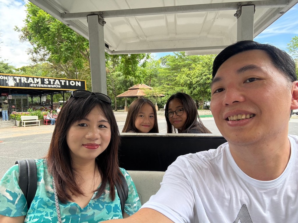 Family taking a group selfie while riding a rented golf cart at Khao Kheow Open Zoo in Chonburi, Thailand